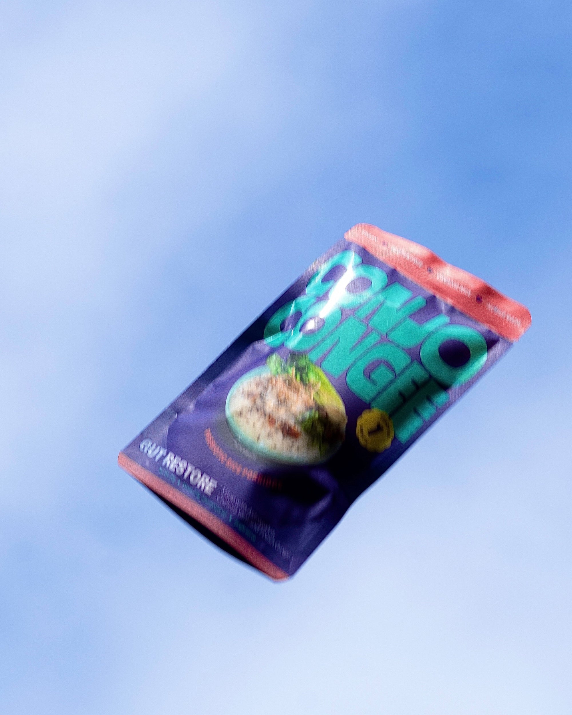 Freeze-dried Conjo Congee ‘Gut Restore’ instant porridge pouch photographed mid-air against a bright blue sky, highlighting its lightness and portability.
