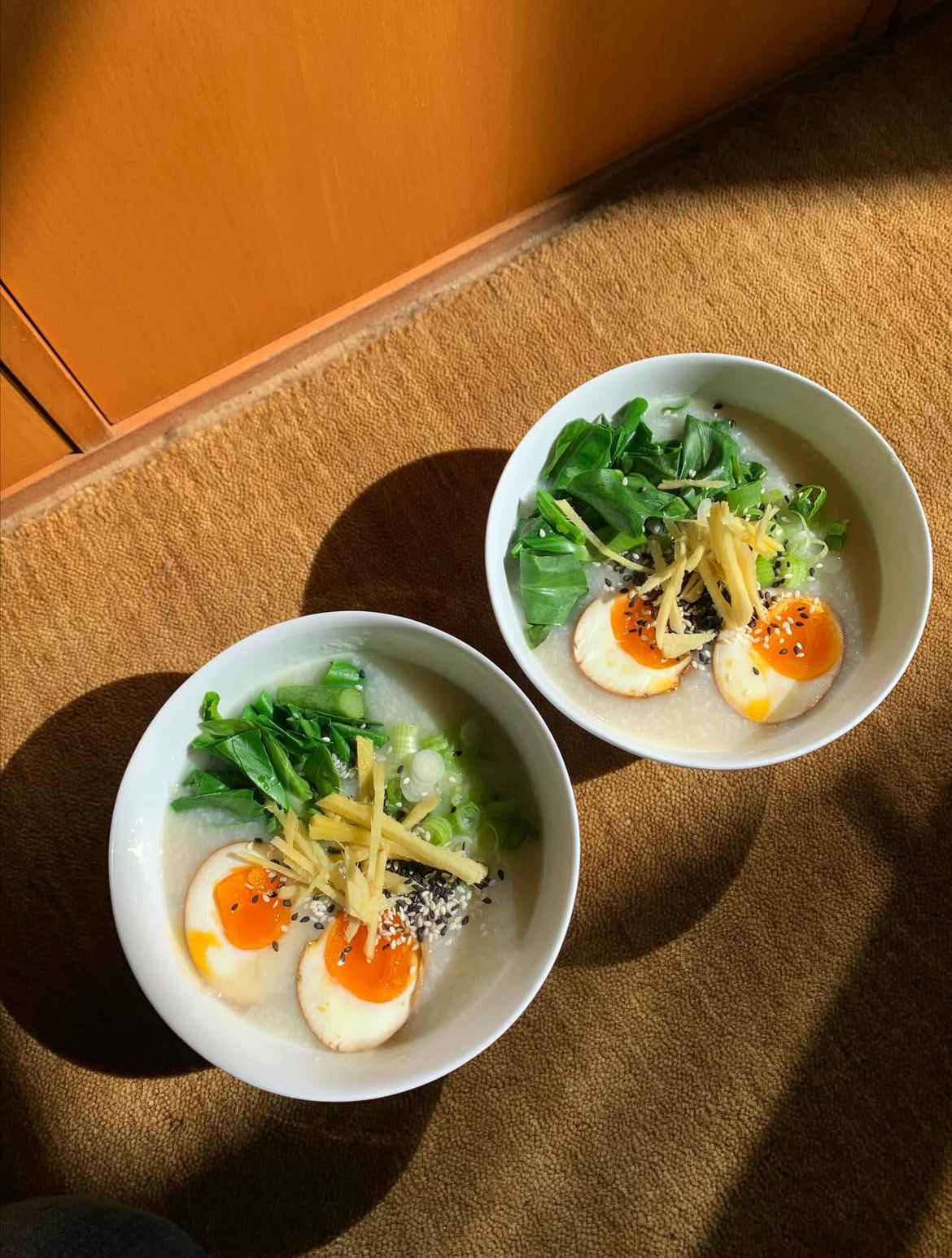 A warm bowl of congee topped with soft-boiled eggs, ginger, and greens — a gut-friendly breakfast that supports protein absorption - Photo by @herby.acupuncture